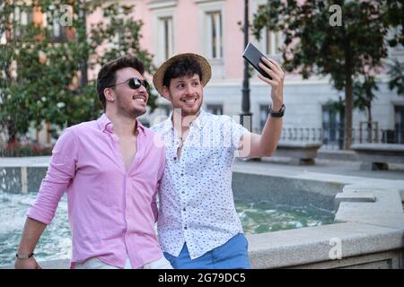 Couple of tourist smiling and taking a selfie at fountain in a city square. Stock Photo
