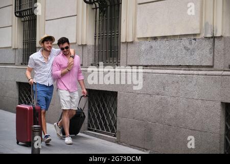 Gay couple carrying suitcases and going to the hotel embraced in a city street. Stock Photo