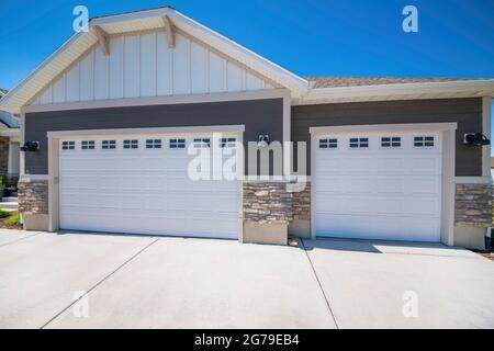 Home exterior with white double garage doors with windows and half stone walls Stock Photo