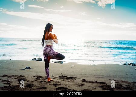 woman in sport clothes practicing yoga and meditating on beach in morning Stock Photo