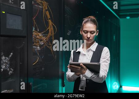 Waist up portrait of female network engineer using digital tablet while setting up servers in data center, copy space Stock Photo