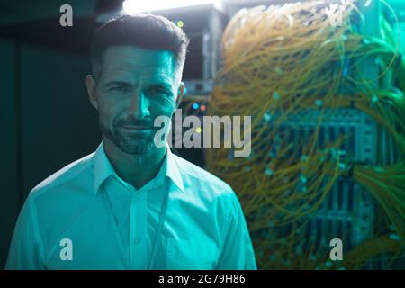 Portrait of handsome data engineer smiling at camera in server room while working with supercomputer in blue light, copy space Stock Photo