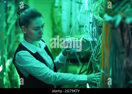 Side view portrait of female network technician working with servers in data center, copy space Stock Photo