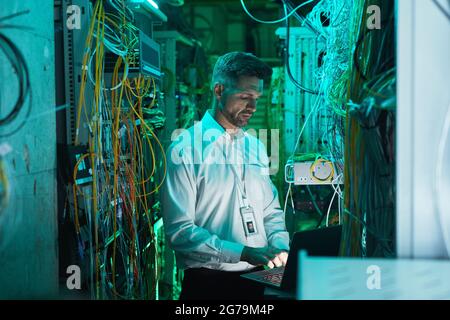 Waist up mature network technician using laptop in server room while working with supercomputer in data center, copy space Stock Photo