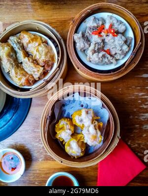 Top View of Delicious Chinese Dim Sum in Bamboo Steamer with Chili Oil and Soy Sauce. Stock Photo