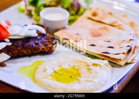 Chargrilled Minced Lamb with Hummus, Pitta Bread and Salad in White Plate. Authentic Middle Eastern Food from Restaurant Stock Photo