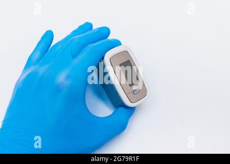 Doctor hand in protective medical gloves holding fingertip pulse oximeter on a white background, closeup. Stock Photo