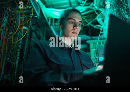 Low angle portrait of young network technician using laptop in server room while setting up supercomputer in data center Stock Photo