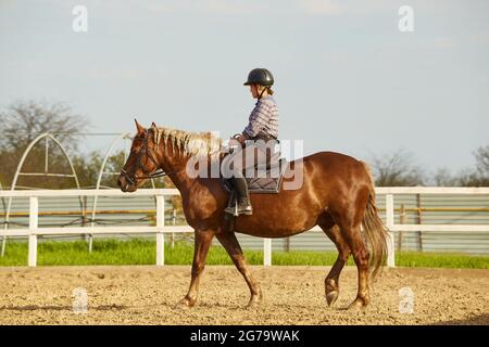 Young girl rides a horse with a light mane Stock Photo