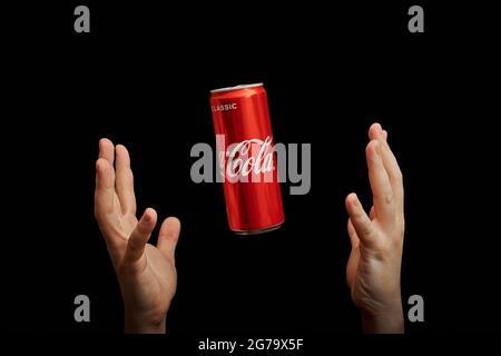 KALININGRAD, RUSSIA - MARCH 13, 2021 - Hands catch Coca Cola can, black background. Classic coke jar, carbonated soft drink. Manufactured by The Coca- Stock Photo