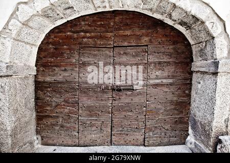 wide two-winged wooden gate, inside a door made of two wings, framed by a stone archway, Lombardy Stock Photo
