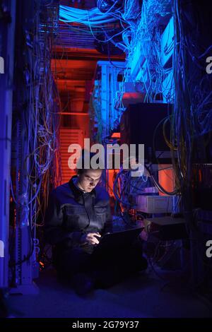 Vertical portrait of young technician setting up internet network in server room Stock Photo