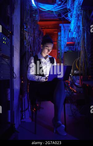 Vertical portrait of young female technician setting up internet network in server room Stock Photo