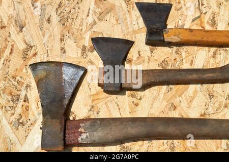 Three old rusty axe tools on plywood background. Stock Photo