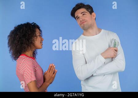 African girl asks her boyfriend for money for her whims, beauty salon and shopping. Husband reluctantly counts her dollar bills. Interracial couple Stock Photo