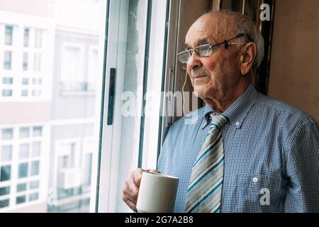 senior man with cup of coffee at home looking out the window Stock Photo