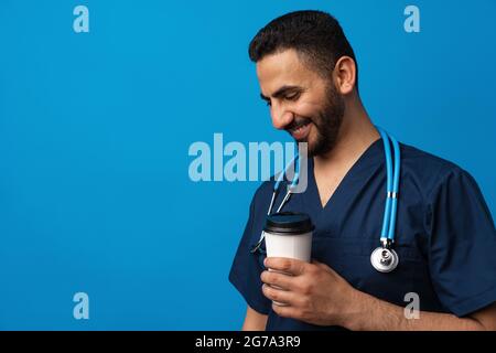 Young arab doctor drinking cup of coffee standing over blue background Stock Photo