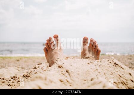 Male feet in sand on beach. Sunbathing, summer vacation, tan concept. Happy tourist rests near sea or ocean. Stock Photo