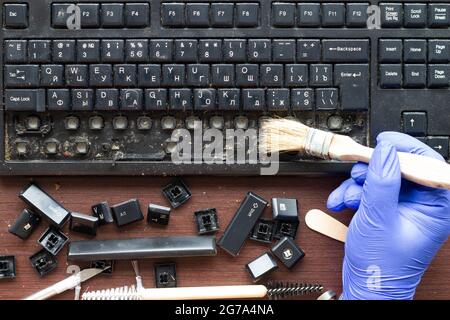 A professional computer electronics technician cleans a dirty computer keyboard with the removed keys with a brush. The tools for repair and cleaning Stock Photo