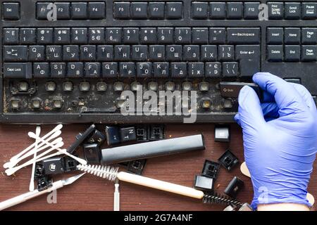 A professional computer electronics technician removes keys from an old, dirty computer wireless keyboard. The tools for repair and cleaning Stock Photo