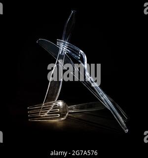 Transparent plastic cutlery, knives and forks against a black background, disposable tableware will be banned to protect the environment and the ocean Stock Photo