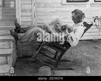 Farmer in rocking-chair reading The Progressive Farmer. 'Farmer reading his farm paper' By George W. Ackerman, Coryell County, Texas, September 1931. Stock Photo