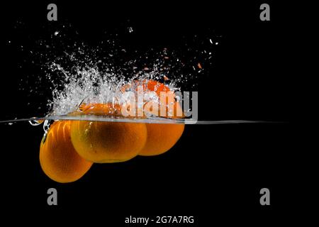 three tangerines fall into the water on a black background, copy space Stock Photo