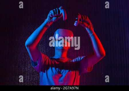 Caucasian man 25-30 years in vr glasses, playing video games with virtual reality headset, trying to touch something with hand in neon light. Stock Photo