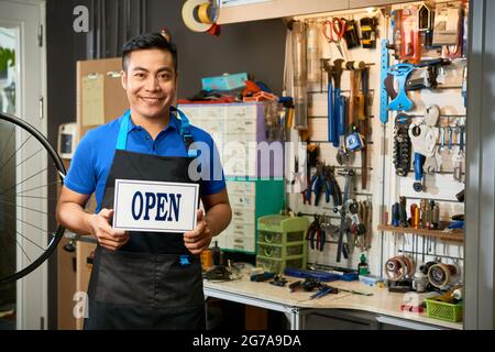 Portrait og happy smiling bicycle mechanic opening workshop and showing signboard Stock Photo