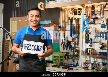 Portrait of smiling mechanic opening workshop and welcoming customers with broken bicycles Stock Photo
