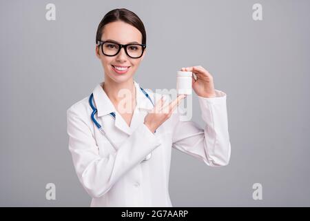 Photo of adorable positive young lady doctor workwear glasses smiling holding pills bottle isolated grey color background Stock Photo