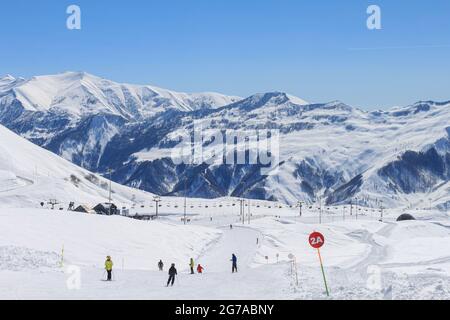 Red ski track with skiers. Against the background of snow-capped peaks and blue sky. The concept of active winter recreation Stock Photo