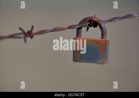 Rusted padlock hangs on barbed wire, symbolic image of captivity, Stuttgart, Baden-Wuerttemberg, Germany Stock Photo