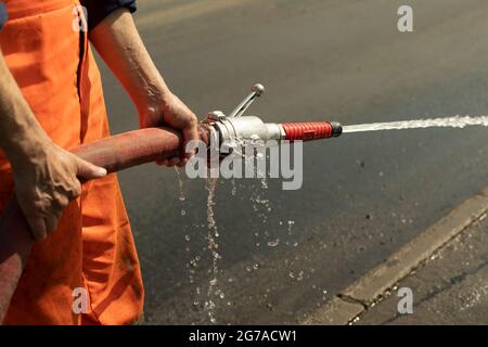 A worker washes the road with a hydrant. Hose with water jet. Washing away dirt from the road. Stock Photo