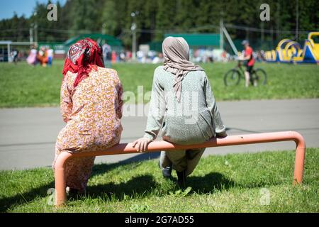 Two Muslim women in headscarves. Women rest in the heat. Women sit with their backs to the camera. Stock Photo