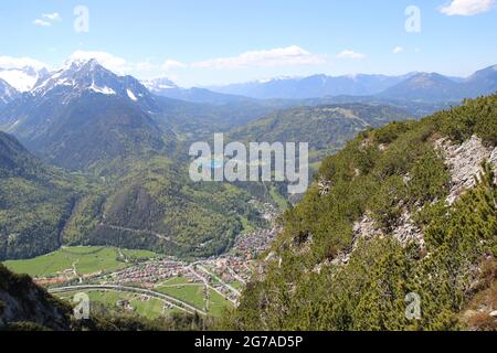 View from the Gamseck above the Mittenwalder Hütte, overview of the Mittenwald area, the Wetterstein Mountains on the left, the Kranzberg in the middle, the Lautersee in between, in spring against a blue sky, woken atmosphere, atmospheric, the Ester Mountains in the background Stock Photo