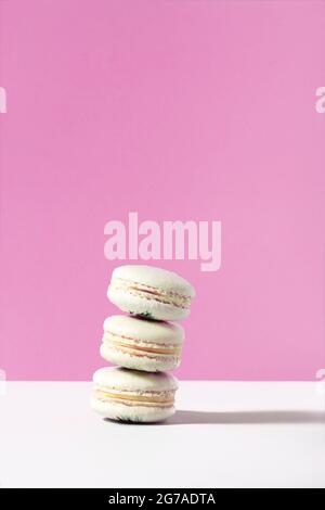 Stack of three white vanilla macarons on pink backdrop. French sugar and almond cookie. Sweet vertical abstract dessert background with space for text Stock Photo