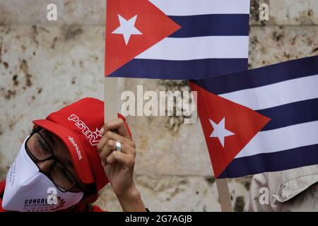 Caracas, Venezuela. 12th July, 2021. A woman wearing a PSUV cap and mouth-nose covering waves flags of Cuba during a rally in front of the Cuban Embassy in support of the island's government. Scores of people had demonstrated the day before in Havana and several other Cuban cities against scarcity and oppression. Observers spoke of the largest demonstrations in Cuba in decades. Credit: Jesus Vargas/dpa/Alamy Live News Stock Photo