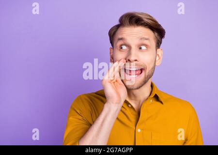 Photo of funny tricky young gentleman dressed yellow shirt arm mouth looking empty space isolated violet color background Stock Photo