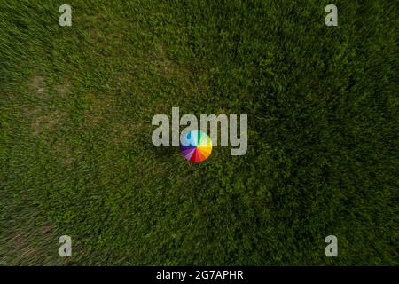 A person is standing in a field with an umbrella painted in rainbow colors Stock Photo