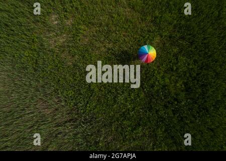 A person is standing in a field with an umbrella painted in rainbow colors Stock Photo