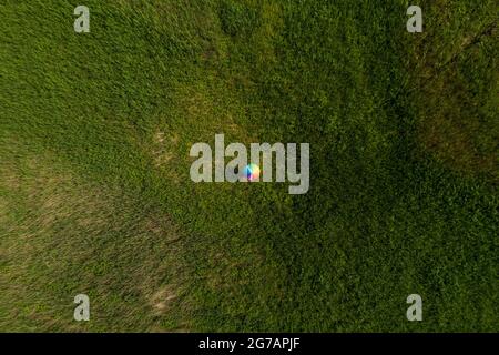 A person is standing in a field with an umbrella painted in rainbow colors Stock Photo