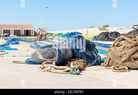 Calpe Spain- August 24 2016; Fisherman drying and mending his blue fishing nets spread out along wharf Stock Photo