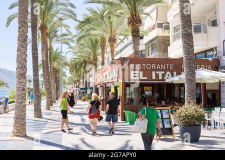 Calpe Spain- August 24 2016; Typically Mediterranean street in tourist coastal town people waliking along street lined with palm trees past restaurant Stock Photo