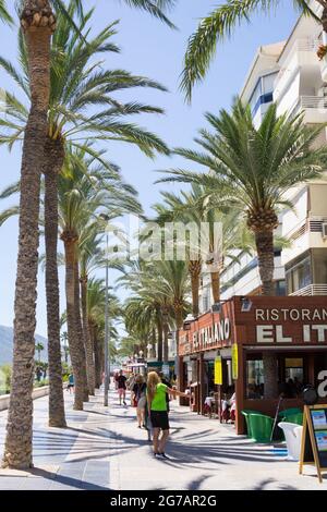 Calpe Spain- August 24 2016; Typically Mediterranean street in tourist coastal town people walking along street lined with palm trees past restaurants Stock Photo