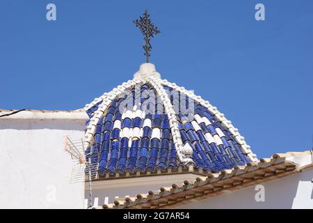 Typical Mediterranean blue and white dome with ornate black wrought iron cross under clear blue sky. in tourist coastal town of Calpe on Costa Blanco. Stock Photo