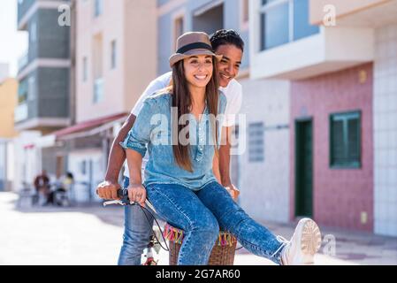 Interracial couple have fun together riding a bike in outdoor in the city - happiness and joy young people interracial boyfriend and girlfriend - two enjoy active lifestyle and love or friendship Stock Photo