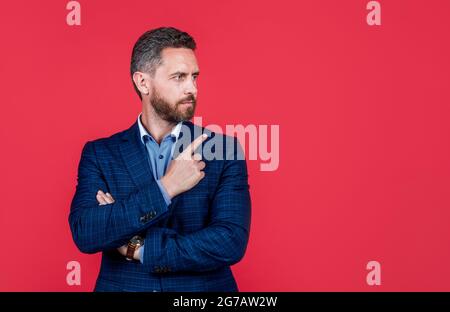 mature ambitious man businessman in businesslike suit pointing finger on copy space, suggestion Stock Photo