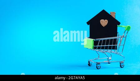 Model of a house in a mini cart on a light blue background with space for text. Investments in residential real estate. Real estate staircase concept, Stock Photo