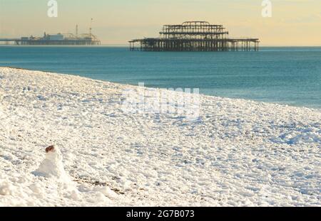 Snow on the beach, Brighton, England, with the Palace Pier and remains of the West pier behind. Focus on Snowman on the beach Stock Photo
